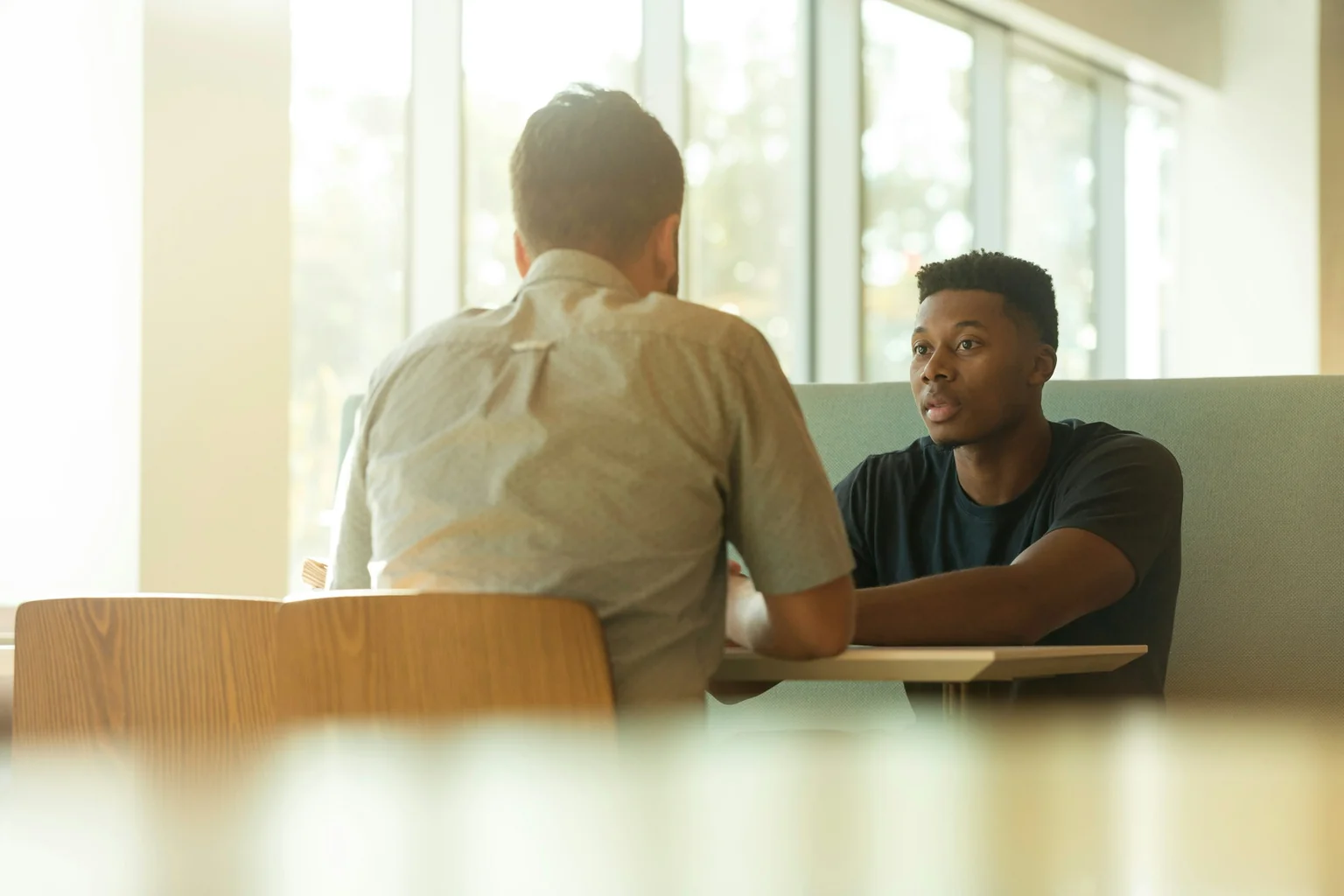 Two people having a focused conversation across a table by a window.