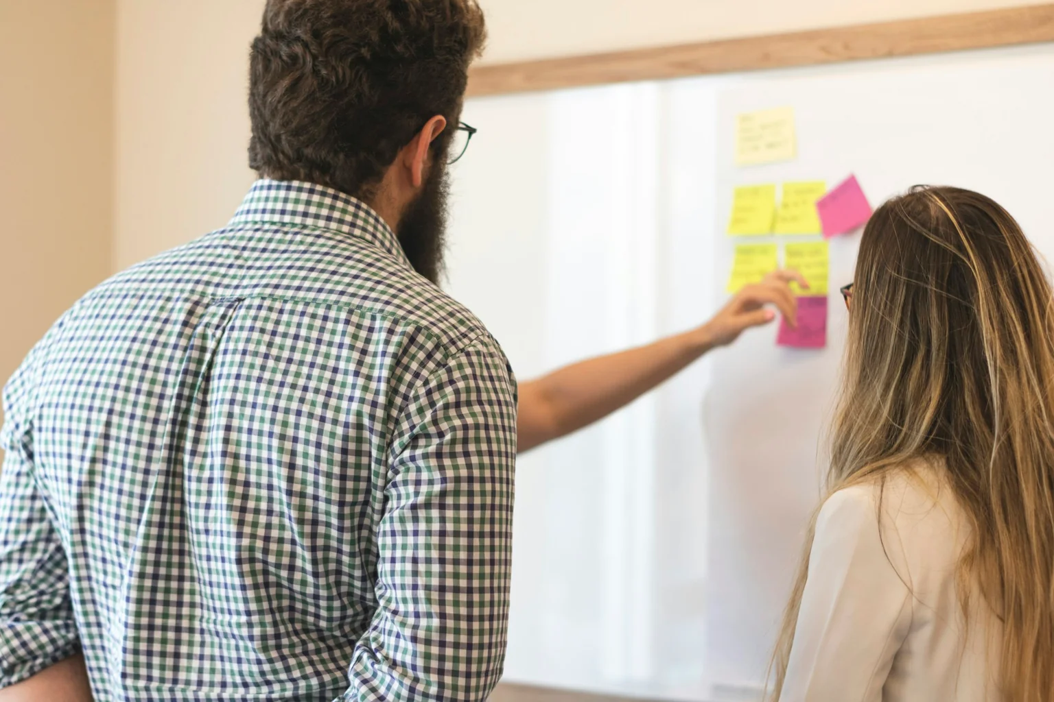 Two workshop participants discussing ideas on a whiteboard with sticky notes.